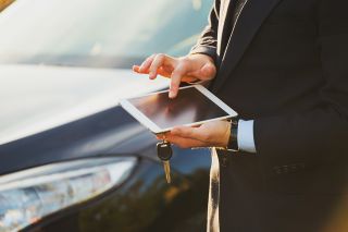 Foto: Person bedient Smartphone vor Auto